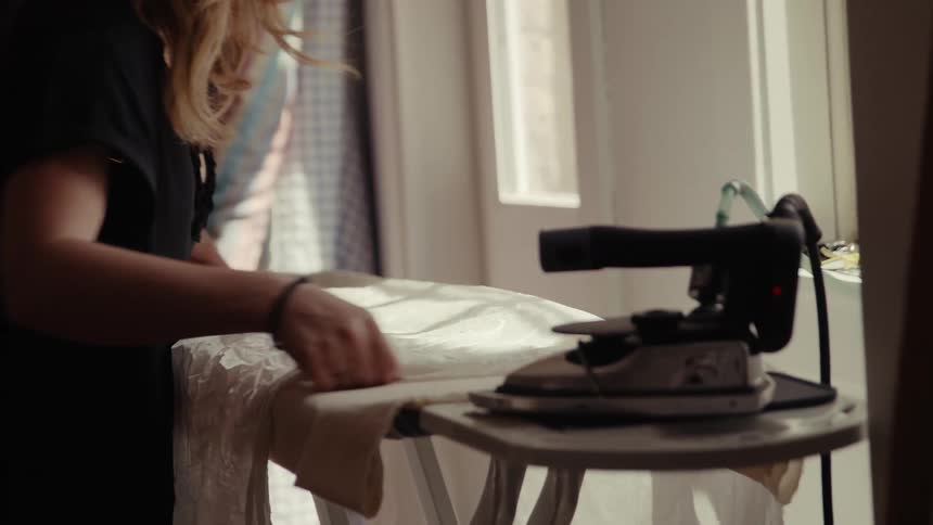 A woman lays a white sheet down on an ironing board