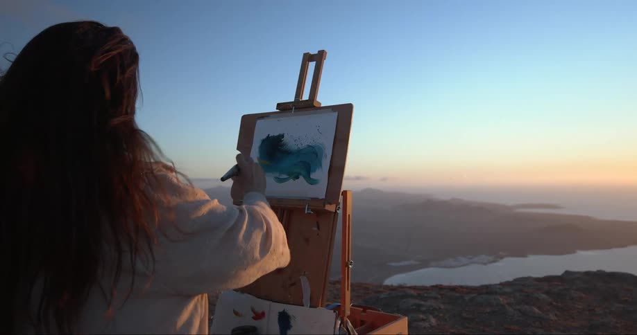 A woman is outdoors and is painting a picture