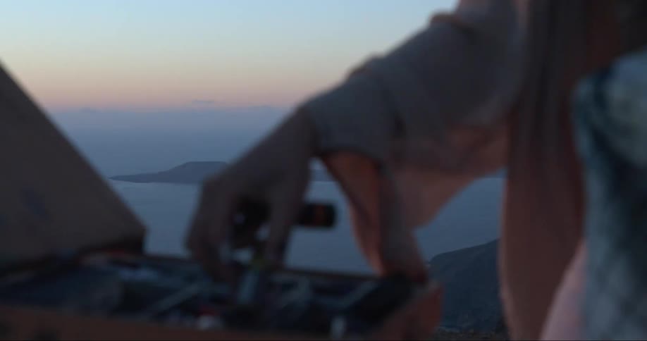 Artist puts sorts items in paint kit while standing on cliff above beach