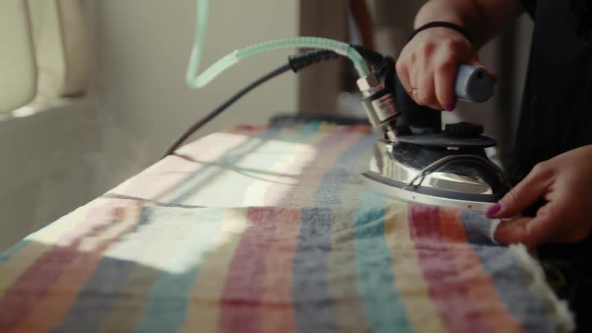 A woman is standing over an ironing board as she irons a piece of stripped cloth and steam rises