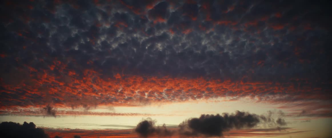 Dark clouds move across the sky with red highlights from the sunlight