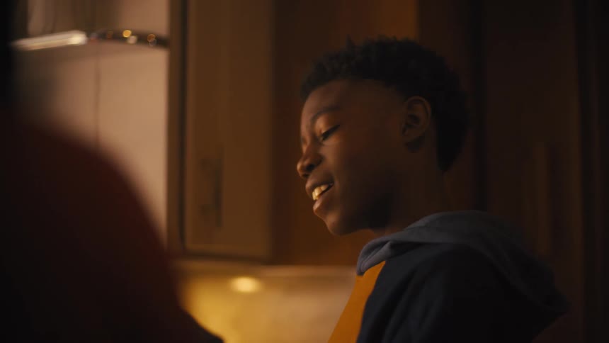 A teenage boy is mixing food in the kitchen with an adult