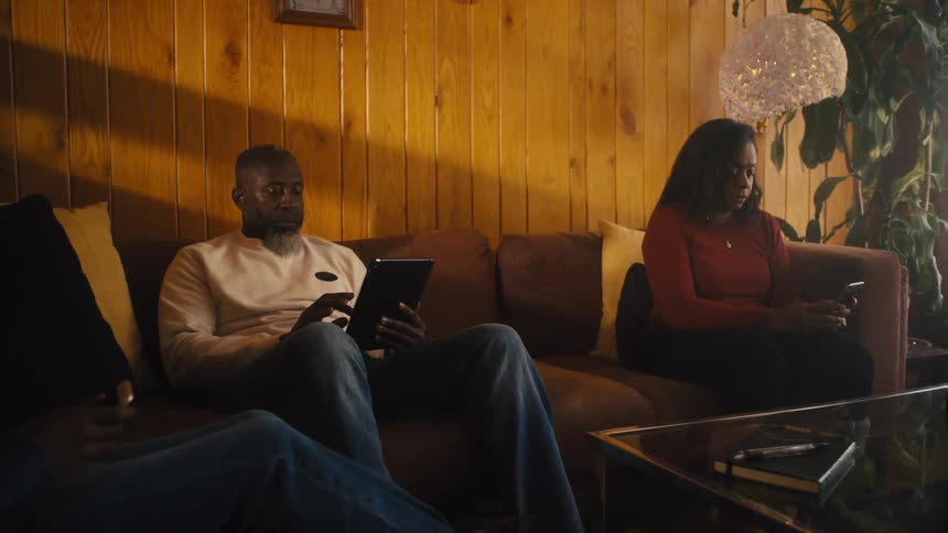 A teenage boy and parents using smartphones and a tablet on a living room sofa