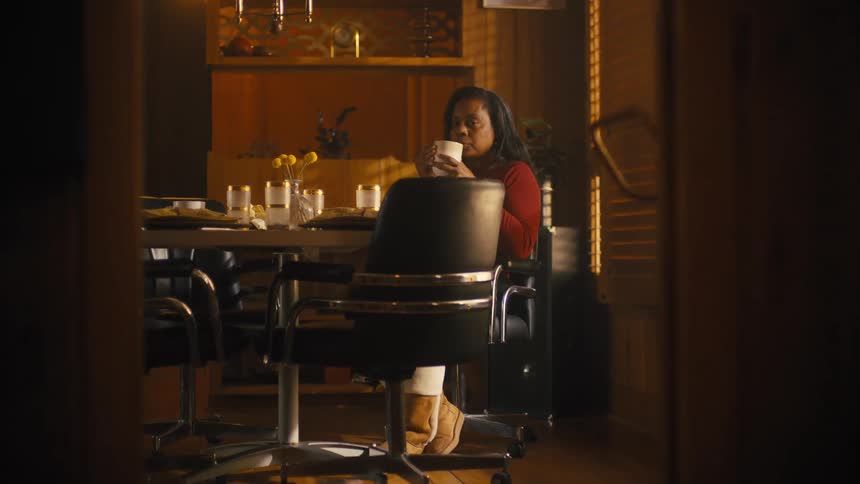 A woman smiling while drinking coffee at a dining table at home