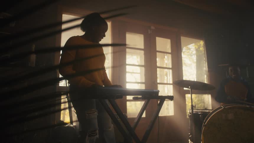 Two people pay keyboard and drums in room together