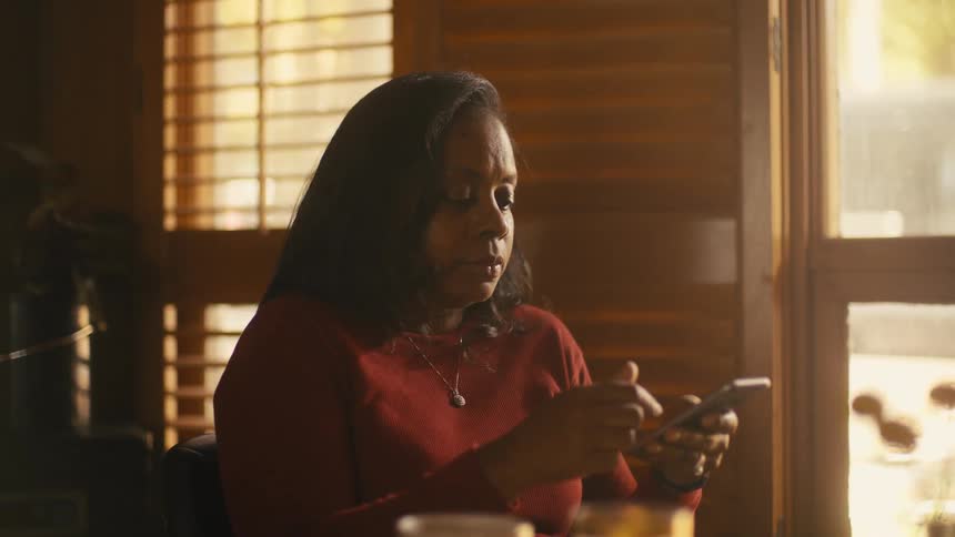 A woman scrolls through her phone while sitting at home