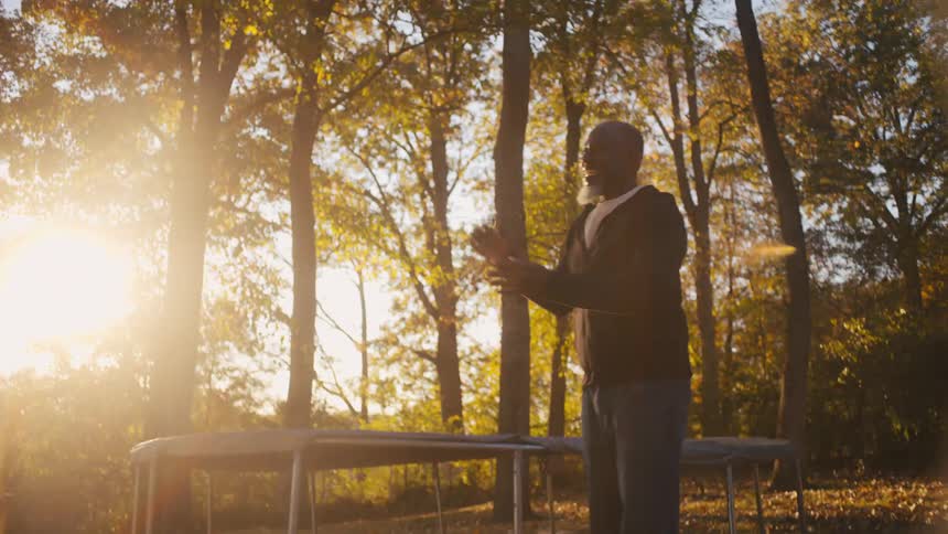 A father and son toss a football outside under trees covered in fall leaves