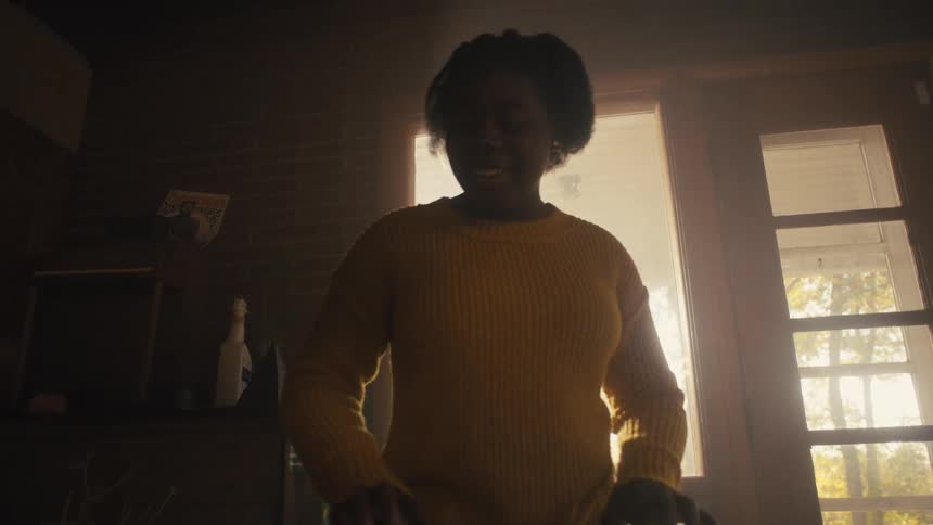 A woman is standing inside singing and playing an electric keyboard as the sun shines brightly in the windows
