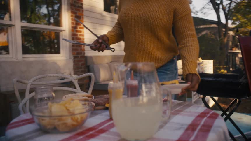 A teenage girl brings a plate of burgers to the table as her dad smiles behind her