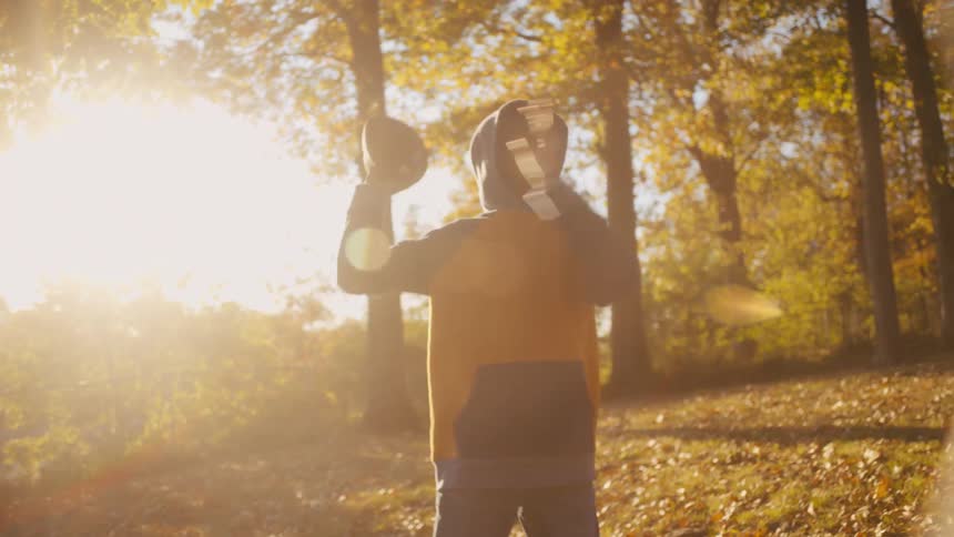 A teenager is catching and throwing a football in a yard with falling leaves