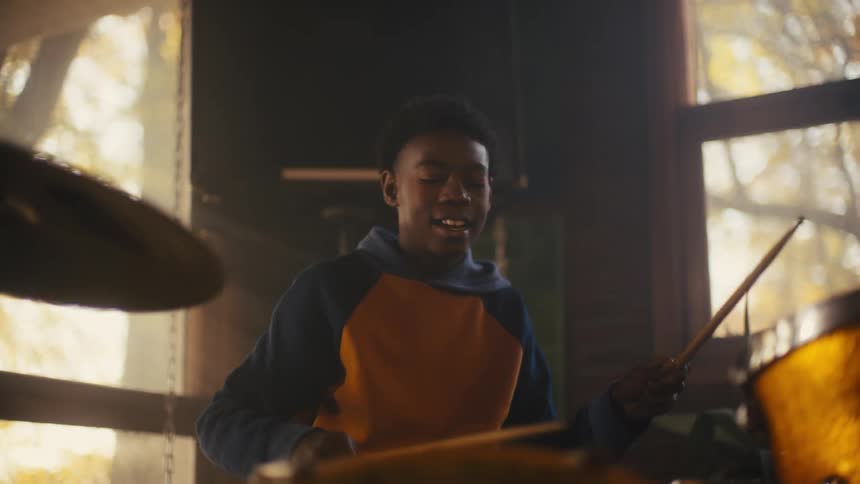 A teenage boy smiles as he plays the drums