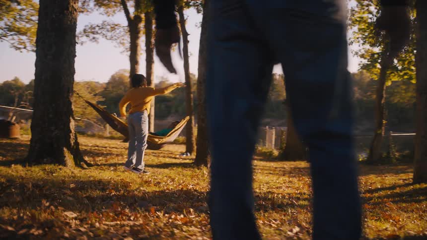 A family is outside in their yard playing catch with a football as their mother relaxes in a hammock