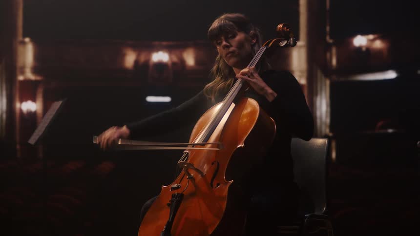A woman is in a theater alone playing a cello