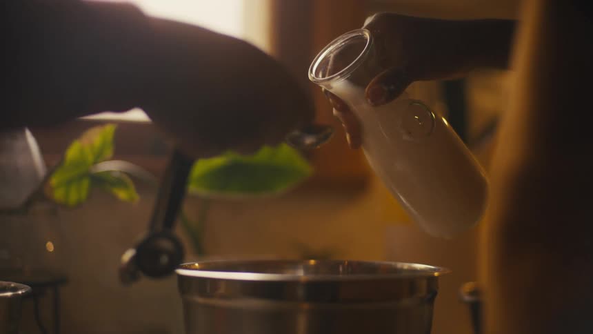 Two people cook together in kitchen working to measure milk into the mixing bowl