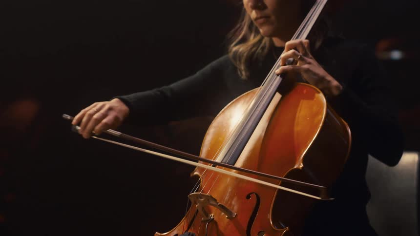 Woman sits playing cello on stage in empty theater