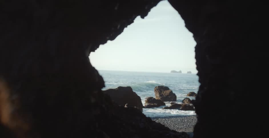 A photographer is taking a picture of the waves rolling in on a beach through a hole in a cave