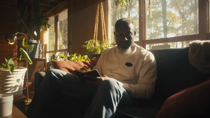 A man sitting on a cup of coffee while writing in a notebook on his living room sofa