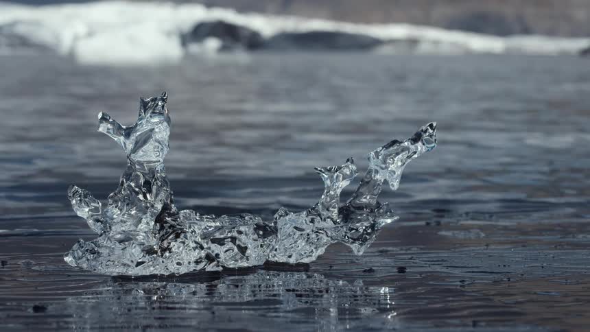 A piece of melting ice sits on the edge of an ice sheet as water ripples and the river flows