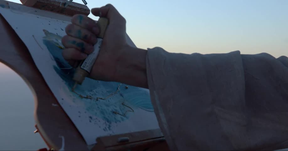 An artist putting paint on a canvas while painting outside at sunset