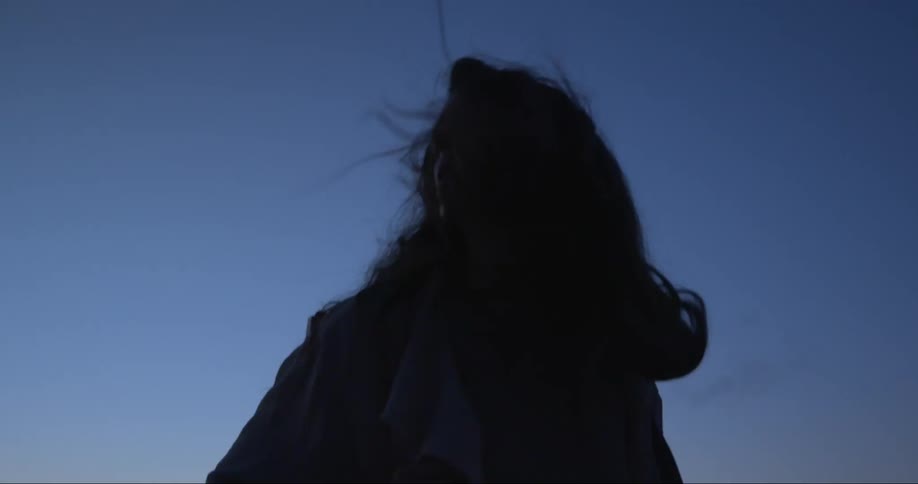 A silhouetted woman spinning around outside with a breeze blowing through her hair
