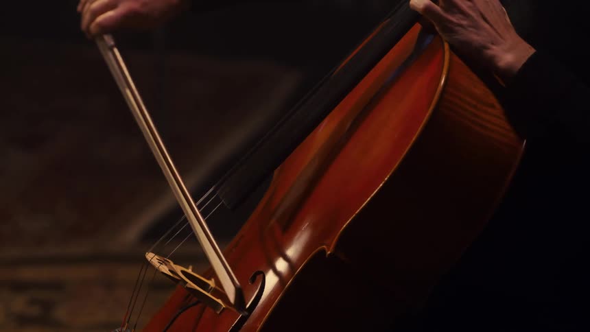 A woman in a black shirt sits and plays the cello