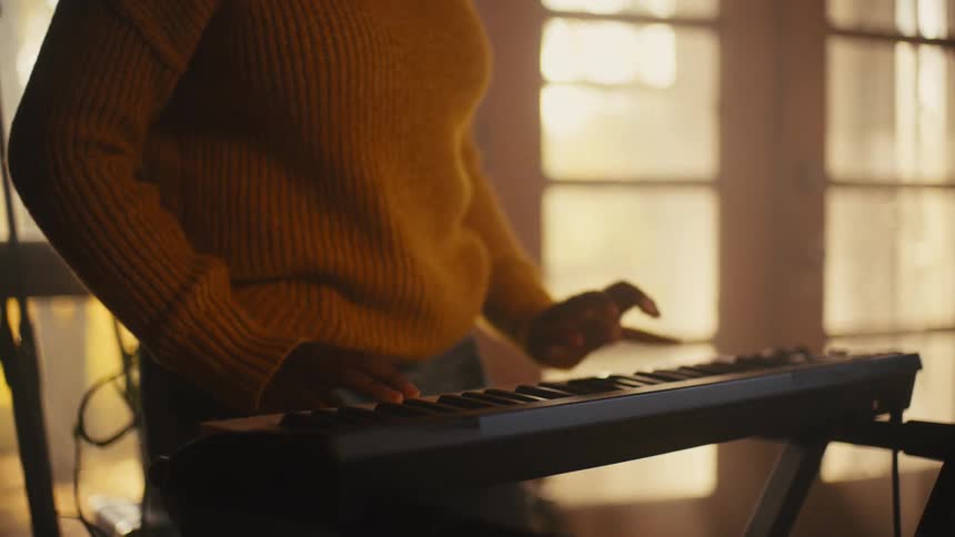 Woman with curly hair and sweater plays electronic keyboard laughing