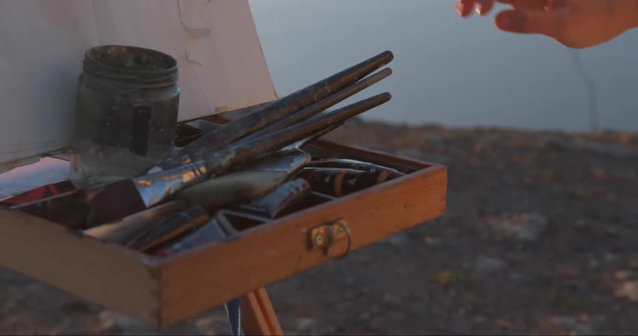 A woman puts paint brushes in a drawer on the easel