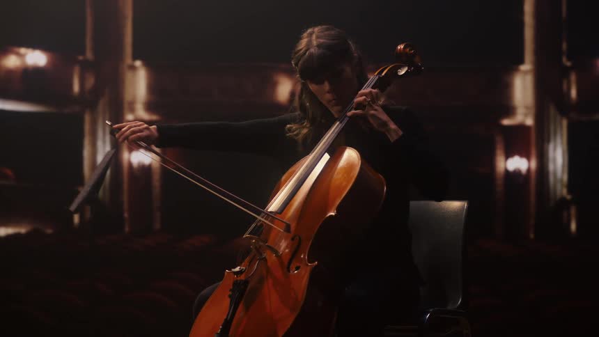 A cellist plays a cello on a stage in an empty theater