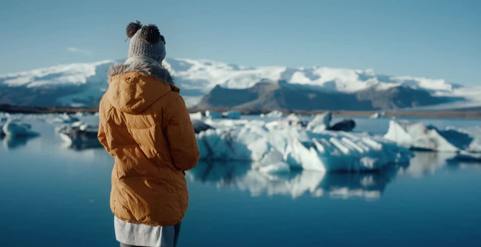 A woman in a winter coat and hat overlooking a body of water with snow and ice
