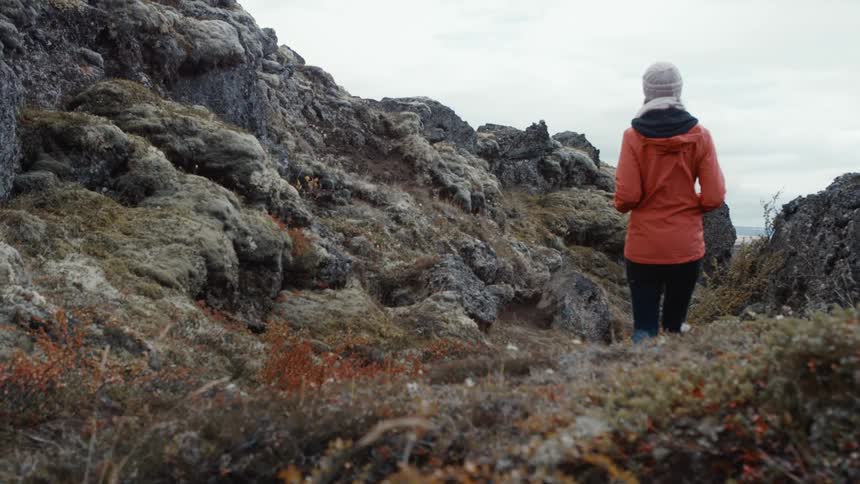 Woman wearing orange jacket hiking on a mountain trail