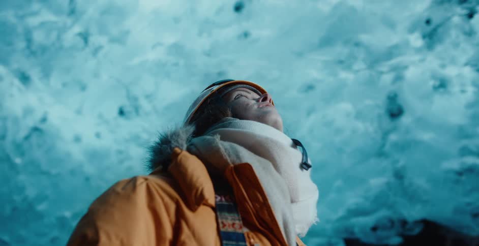 A woman in a helmet and coat looking up at an ice cave