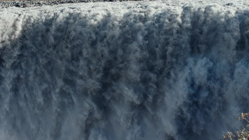 River waters flow down waterfall near rocky mountain and wildflower covered cliff top