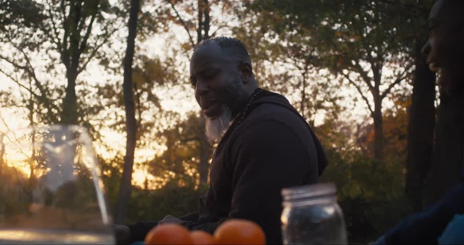 A man is sitting outside nodding his head as he speaks and bumps fists with his son