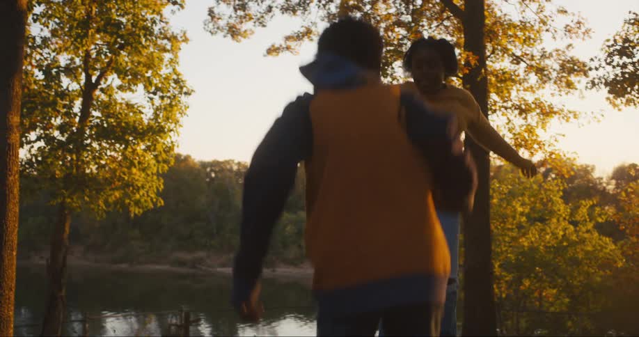 Boy and girl jump up and down on trampoline near the lake at sunset