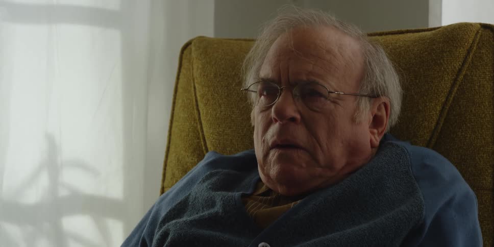 Elderly man carrying glass sits in chair breathing tiredly