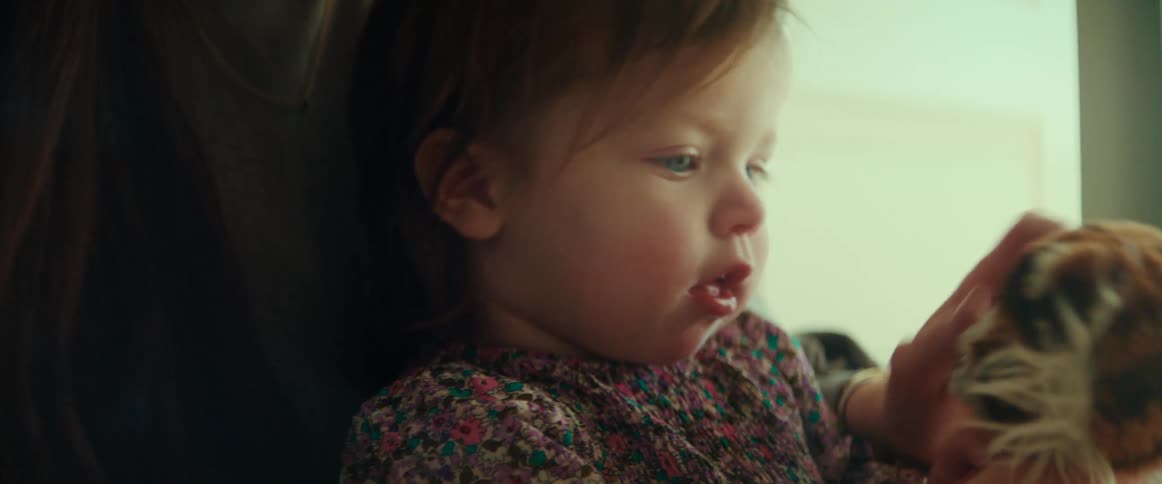 A baby girl plays with a stuffed tiger while sitting in her mothers lap