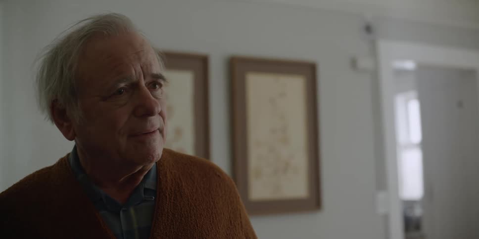 A man is standing in his living room thinking for a moment as a woman walks out of the room and he leaves