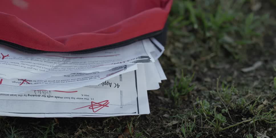 Filled forms spill out of backpack lying on the ground