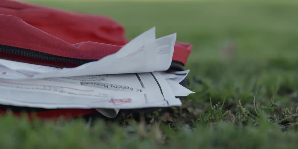 School papers in a bag lying in the grass as the wind blows them