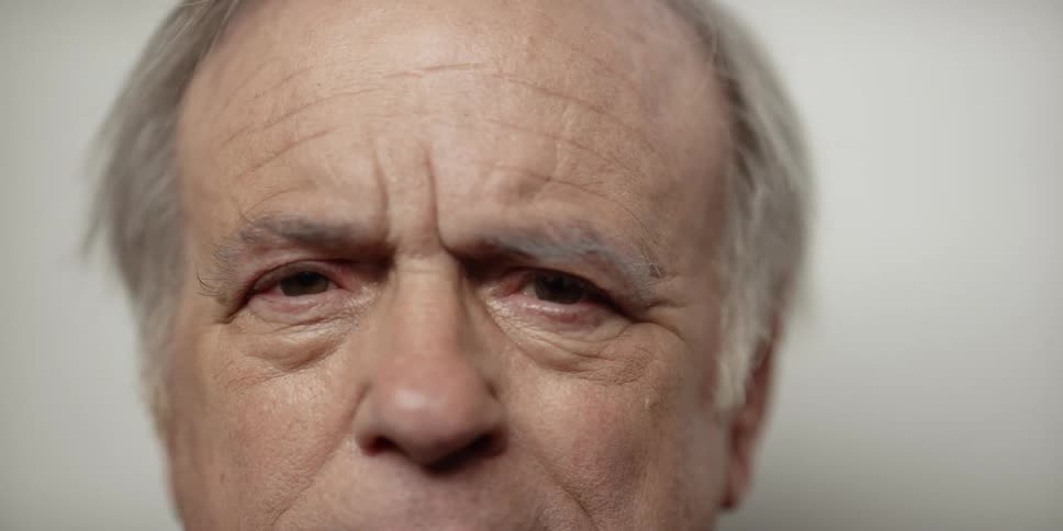 Elderly man with gray hair and wrinkles stares at camera