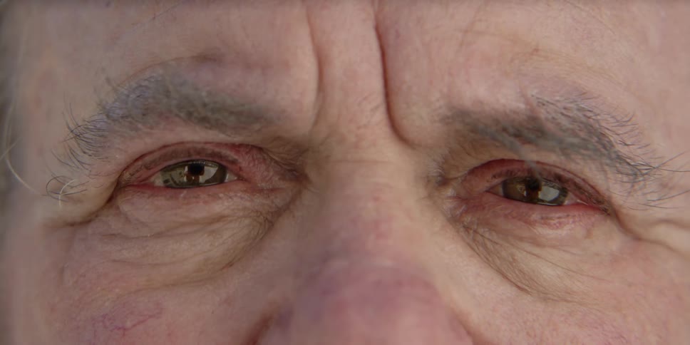 An elderly man blinks as he stares straight ahead