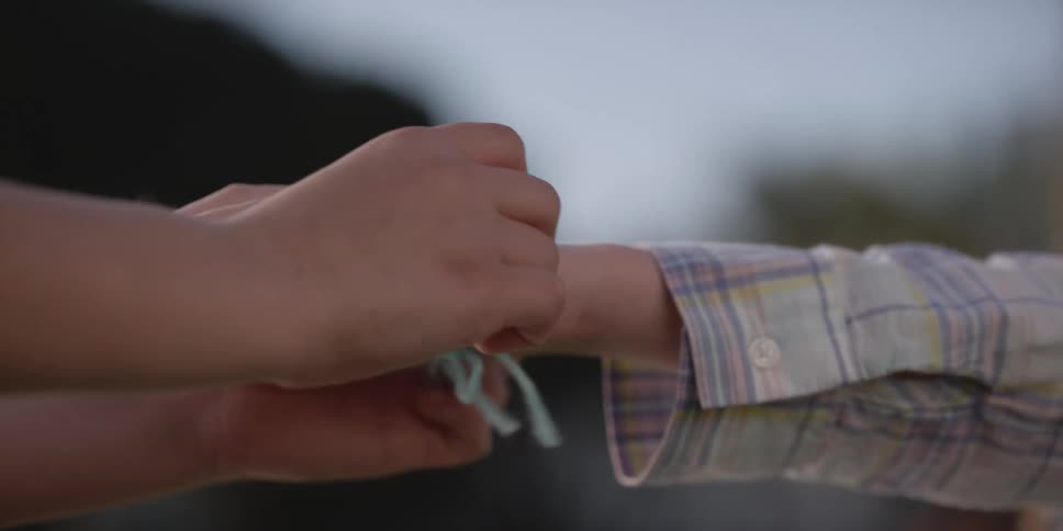 A boy puts a braided friendship bracelet on his friends wrist
