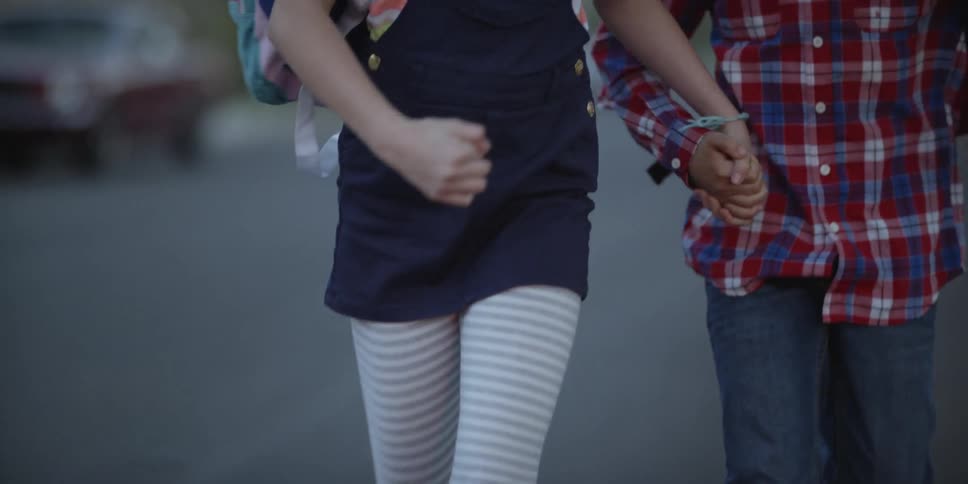 A girl and boy run together down a road while holding hands