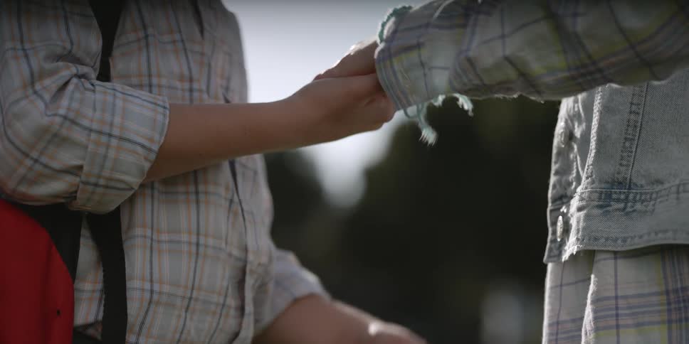 A boy puts a bracelet on a girl's wrist and they run off