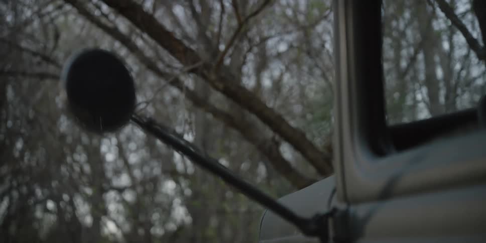 A man carrying a riffle gets out of a truck and follows another man in to a forest