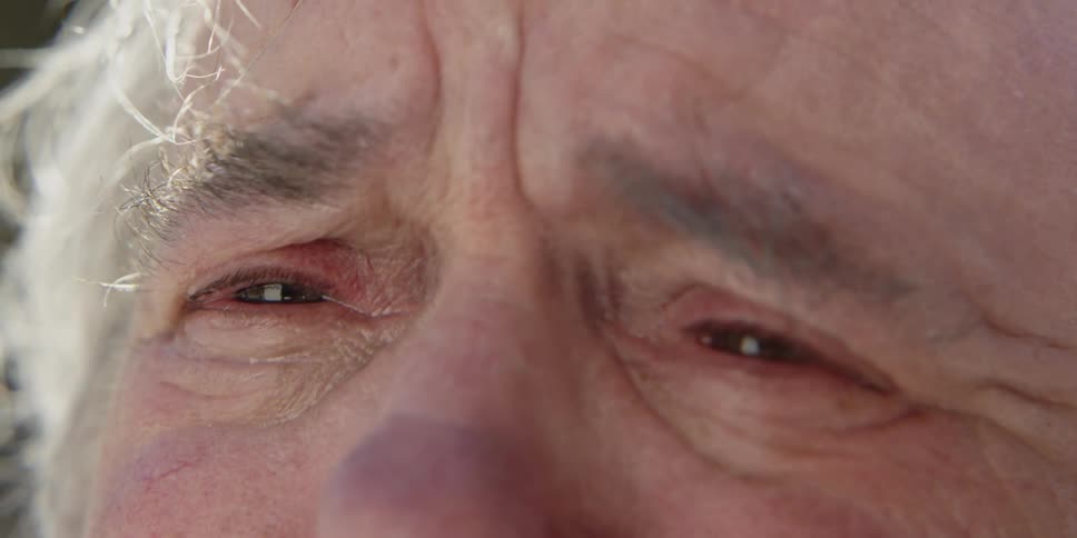 An elderly man is looking into the camera