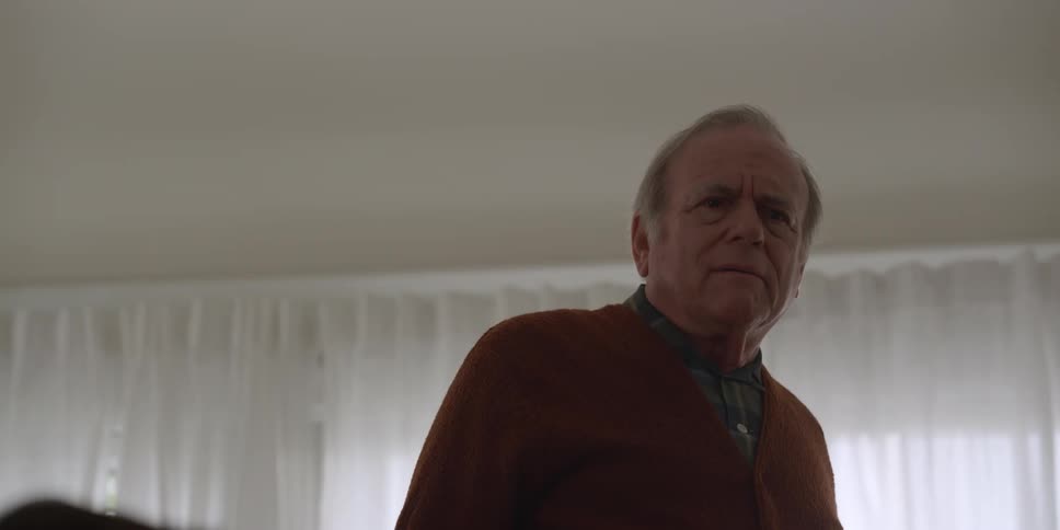 A man is standing in his living room as he turns and speaks to someone and walks away