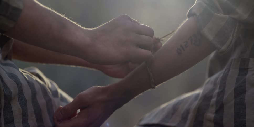 A man holds out his arm as another man ties a string around it