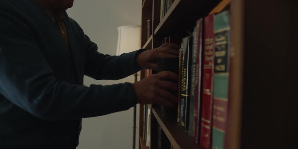 An elderly man at home puts a book on a book case