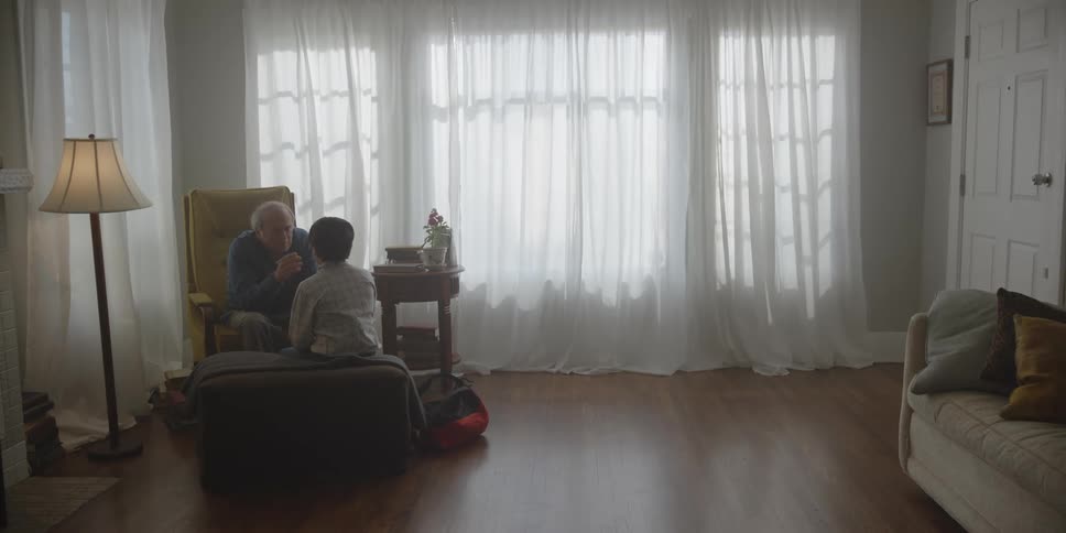 A man is sitting in his living room talking to his young grandson